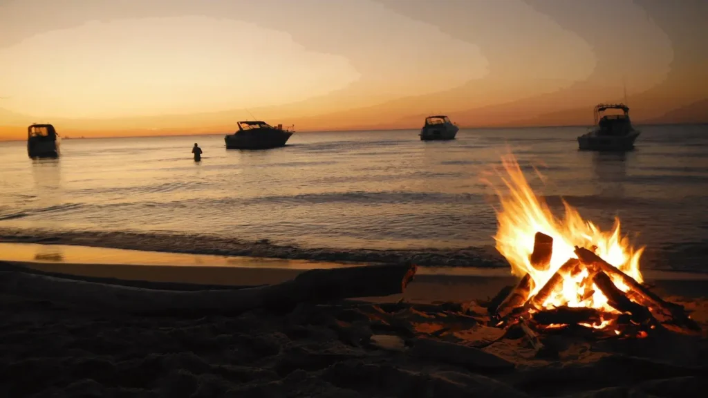 Bonfire on the beach at sunset with boats on the sea during San Juan Night celebration in Spain