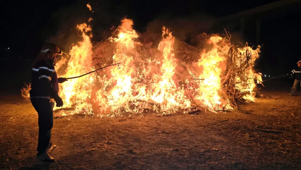 Beach bonfire at night with two firefighters controlling the fire during San Juan Night celebration in Spain