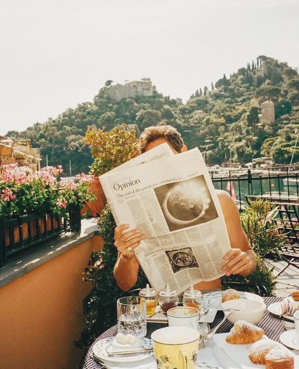 Man reading a newspaper while enjoying breakfast on a sunny Mediterranean terrace surrounded by flowers