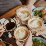 Friends toasting with Spanish Lattes and espresso at a cozy Mediterranean café table