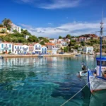 Traditional fishing harbor in Ikaria, Greece, a Blue Zone island known for exceptional longevity, with colorful houses on hillside and wooden fishing boat in turquoise waters